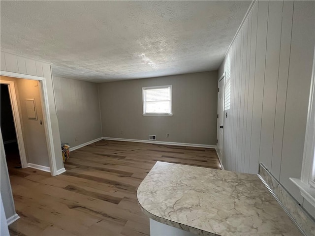 empty room featuring a textured ceiling, light wood finished floors, visible vents, and baseboards