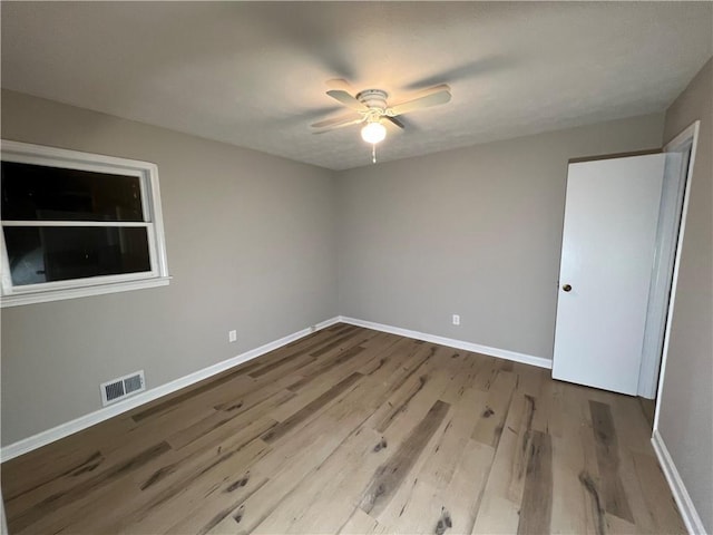 empty room with a ceiling fan, visible vents, baseboards, and wood finished floors