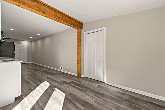 unfurnished living room featuring dark wood-type flooring, recessed lighting, beam ceiling, and baseboards