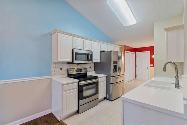 kitchen featuring lofted ceiling, sink, appliances with stainless steel finishes, tasteful backsplash, and white cabinetry