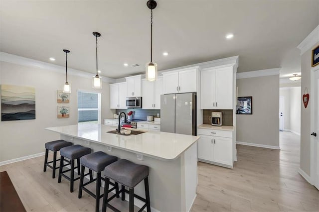 kitchen with sink, white cabinetry, stainless steel appliances, an island with sink, and decorative light fixtures