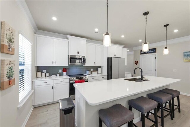 kitchen featuring pendant lighting, sink, appliances with stainless steel finishes, white cabinetry, and a center island with sink