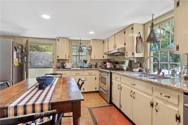 kitchen with light wood-type flooring, cream cabinetry, sink, light stone counters, and stainless steel appliances