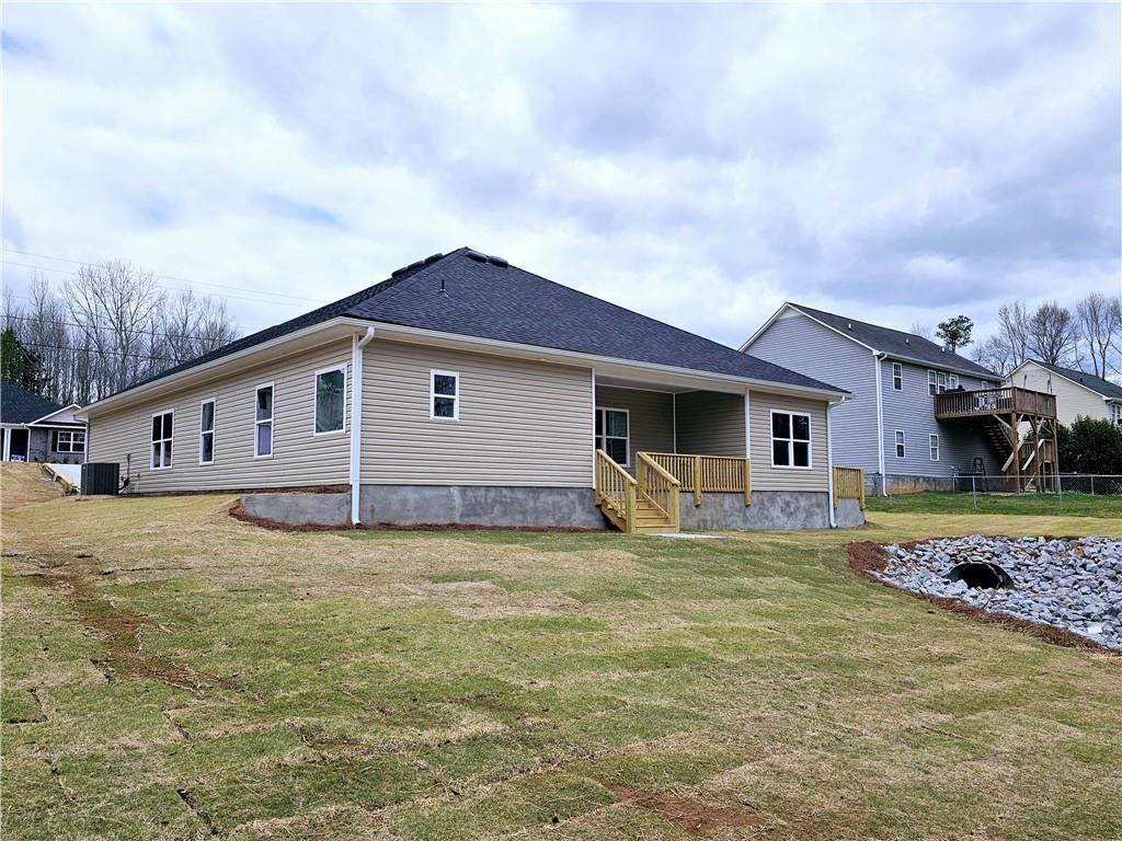 rear view of house with a yard, fence, cooling unit, and a shingled roof