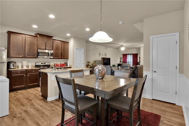 kitchen with pendant lighting, appliances with stainless steel finishes, light hardwood / wood-style floors, ceiling fan, and light stone counters