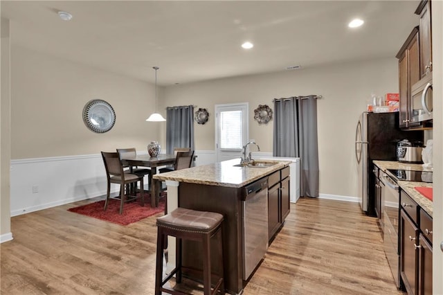 kitchen with pendant lighting, stainless steel appliances, a center island with sink, and light hardwood / wood-style floors