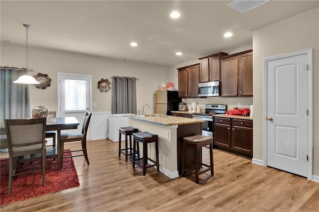 kitchen with decorative light fixtures, stainless steel appliances, light hardwood / wood-style floors, a kitchen bar, and a center island with sink