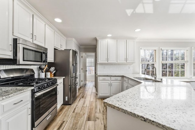 kitchen with white cabinets, stainless steel appliances, crown molding, wood finish floors, and a sink