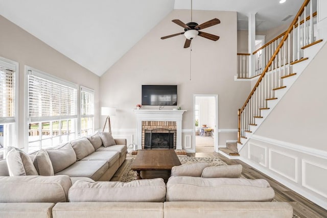 living room with a decorative wall, stairway, a brick fireplace, ceiling fan, and wood finished floors