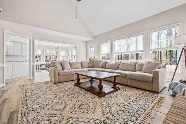 living room featuring light wood-type flooring, an inviting chandelier, and high vaulted ceiling