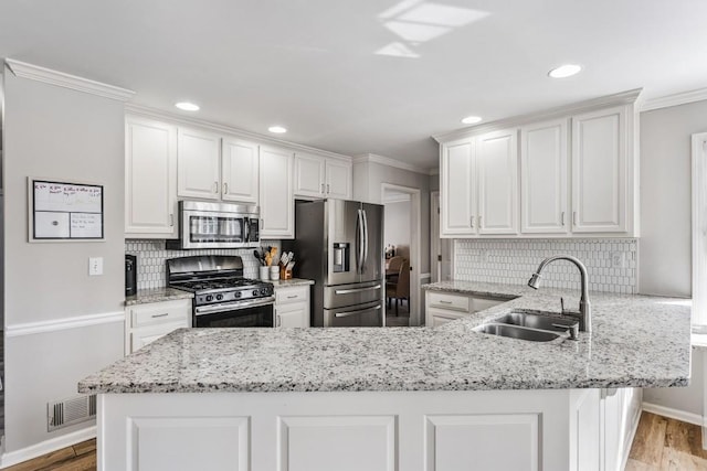 kitchen featuring stainless steel appliances, a peninsula, a sink, white cabinetry, and ornamental molding