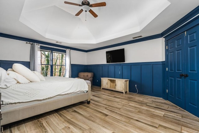 bedroom featuring a tray ceiling, wainscoting, and visible vents