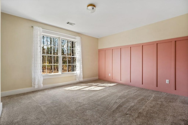 carpeted spare room with visible vents and a decorative wall