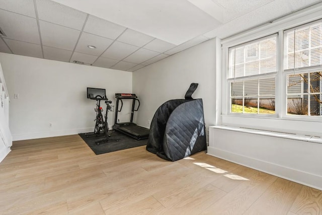 exercise area with a paneled ceiling, light wood finished floors, and baseboards