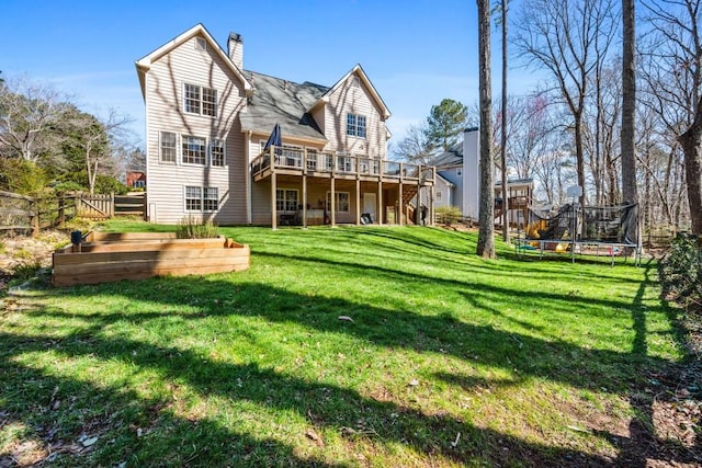 rear view of property with a deck, fence, a yard, a trampoline, and a chimney