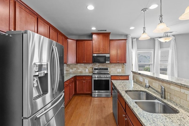 kitchen featuring backsplash, sink, light stone countertops, appliances with stainless steel finishes, and decorative light fixtures