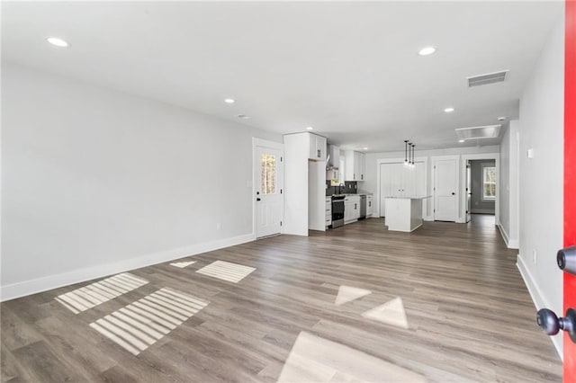 unfurnished living room featuring attic access, visible vents, baseboards, and wood finished floors