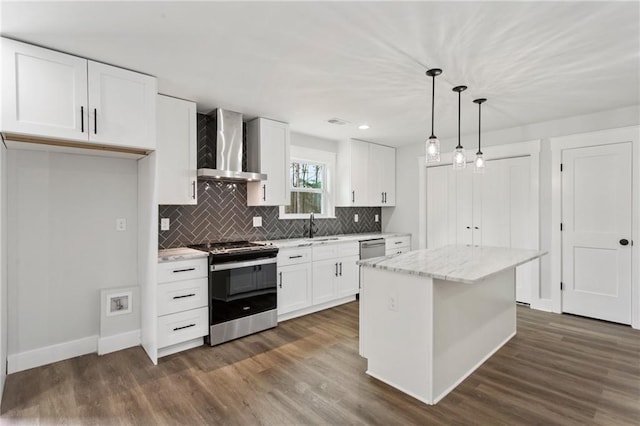 kitchen with a center island, pendant lighting, appliances with stainless steel finishes, white cabinetry, and wall chimney exhaust hood