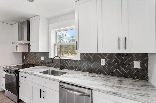 kitchen with stainless steel appliances, white cabinets, a sink, light stone countertops, and wall chimney exhaust hood