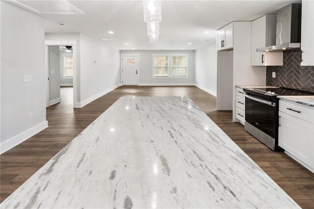 kitchen with light stone countertops, wall chimney range hood, stainless steel electric range, and white cabinets