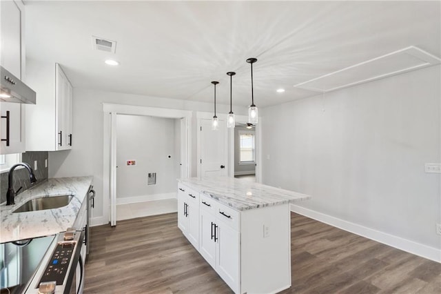kitchen featuring light stone counters, pendant lighting, white cabinetry, a kitchen island, and a sink