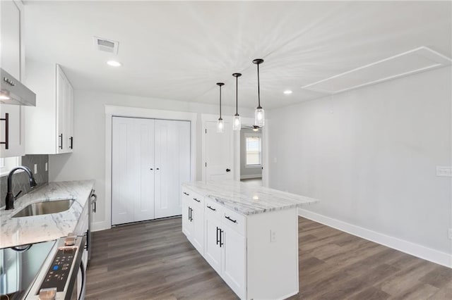 kitchen with pendant lighting, white cabinetry, a kitchen island, a sink, and light stone countertops