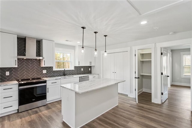 kitchen with wall chimney exhaust hood, appliances with stainless steel finishes, a center island, hanging light fixtures, and white cabinetry