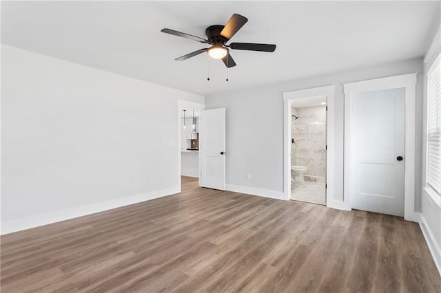 unfurnished bedroom with ceiling fan, connected bathroom, baseboards, and wood finished floors
