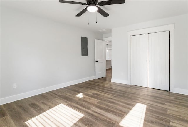 unfurnished bedroom with dark wood-style floors, electric panel, baseboards, and a closet