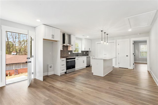 kitchen with white cabinets, wall chimney exhaust hood, decorative light fixtures, a center island, and stainless steel appliances