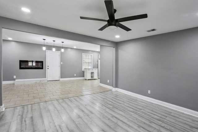 unfurnished living room featuring visible vents, light wood-style flooring, a glass covered fireplace, recessed lighting, and baseboards