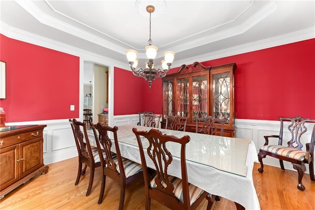 dining space with a raised ceiling, ornamental molding, a notable chandelier, and light wood-type flooring