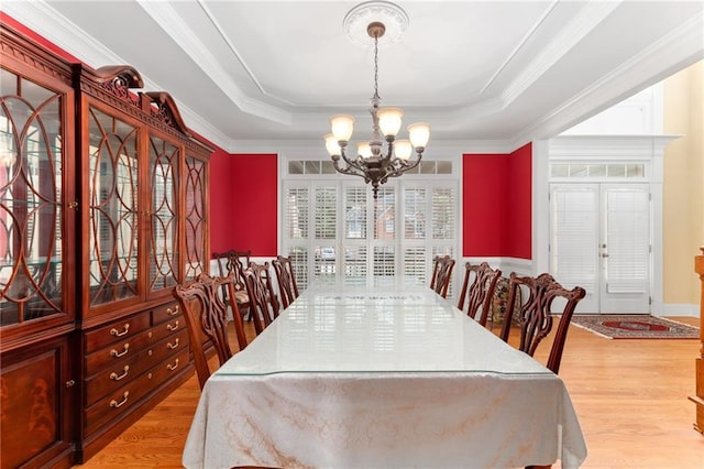 dining area with a raised ceiling, a notable chandelier, and light hardwood / wood-style flooring