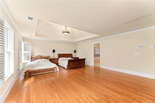 bedroom with light wood-type flooring, crown molding, a tray ceiling, a chandelier, and ensuite bathroom