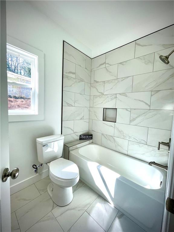 bathroom with bathtub / shower combination, baseboards, marble finish floor, and toilet