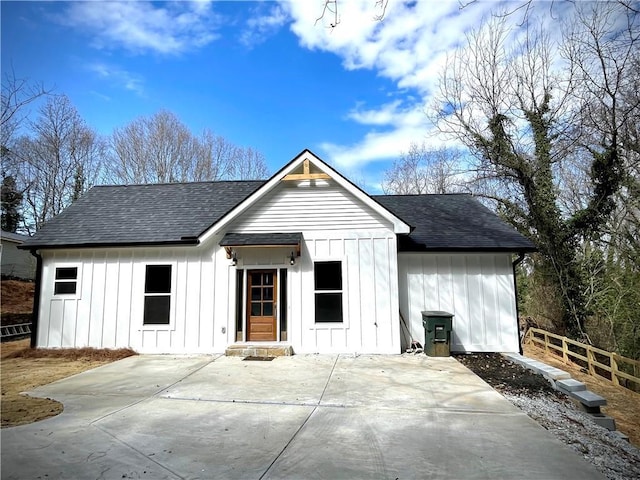 view of front facade with board and batten siding, roof with shingles, a patio, and fence