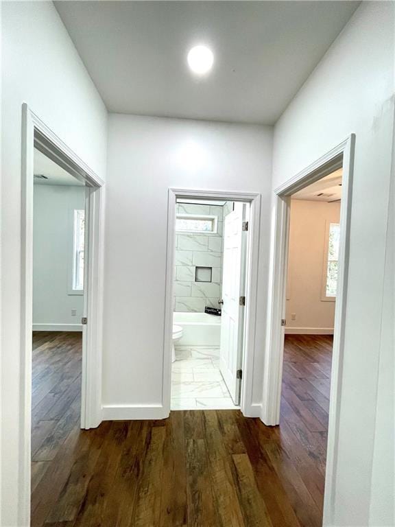 corridor featuring dark wood-type flooring, plenty of natural light, and baseboards