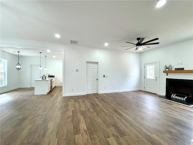 unfurnished living room with baseboards, a fireplace with raised hearth, ceiling fan, wood finished floors, and recessed lighting