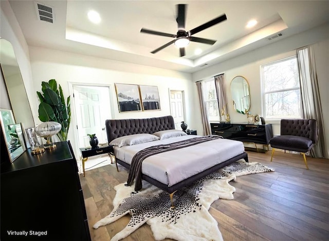 bedroom with wood finished floors, a raised ceiling, and visible vents