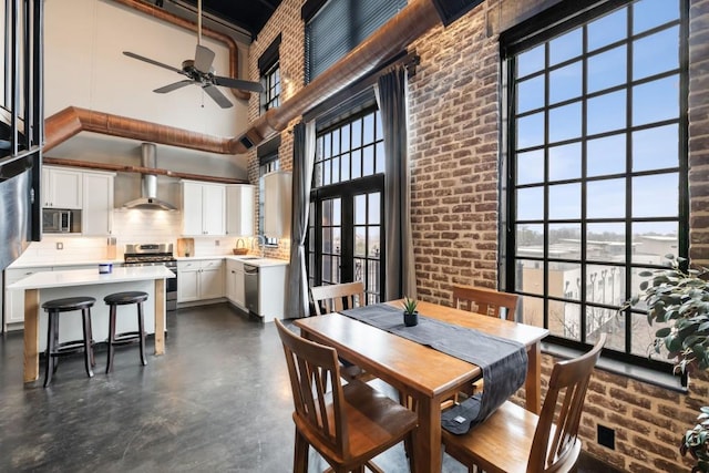 dining area featuring brick wall, a towering ceiling, sink, and ceiling fan