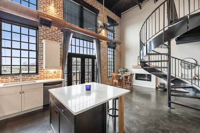 kitchen with white cabinetry, a towering ceiling, a kitchen island, brick wall, and stainless steel dishwasher