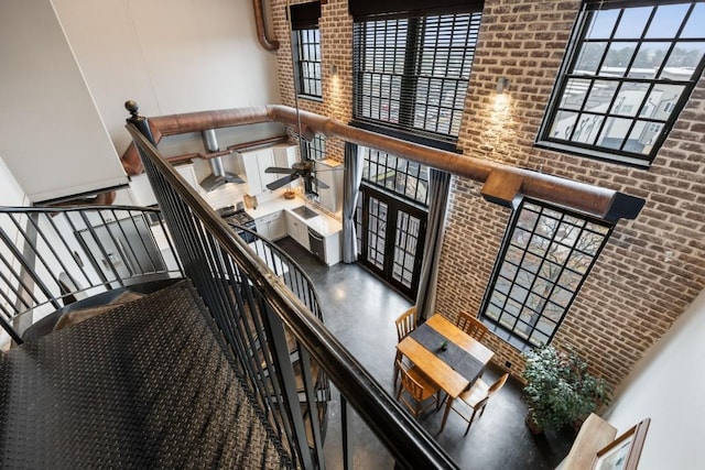 stairway featuring a healthy amount of sunlight, a towering ceiling, and brick wall