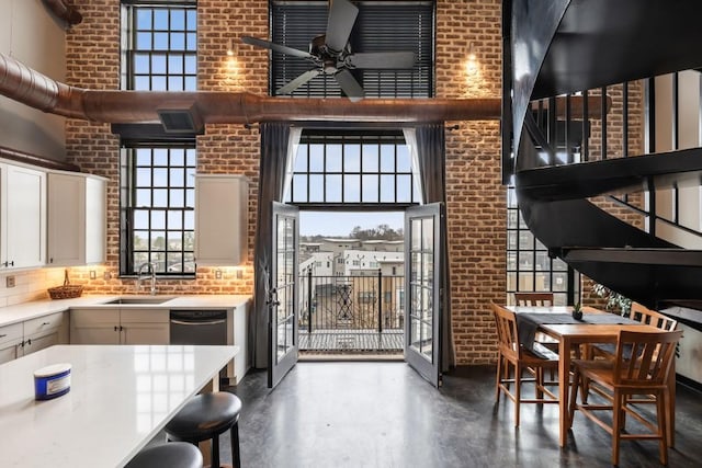 kitchen featuring white cabinetry, brick wall, sink, and a towering ceiling