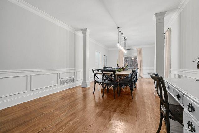 dining space with decorative columns, a decorative wall, crown molding, and wood finished floors