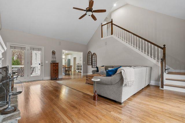 living room with light wood finished floors, ceiling fan, high vaulted ceiling, baseboards, and stairs