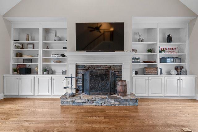 living area with light wood-type flooring, built in features, vaulted ceiling, and a stone fireplace