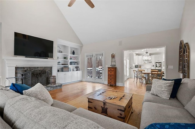 living room featuring high vaulted ceiling, light wood-type flooring, a fireplace, and built in features