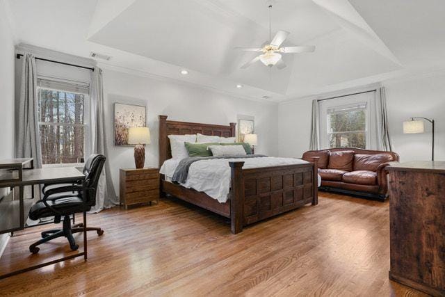 bedroom with light wood-type flooring, a raised ceiling, and multiple windows