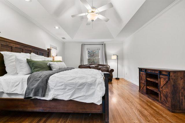 bedroom featuring a tray ceiling, recessed lighting, a ceiling fan, wood finished floors, and baseboards