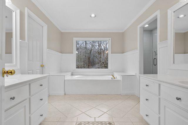 bathroom featuring two vanities, tile patterned flooring, wainscoting, and crown molding